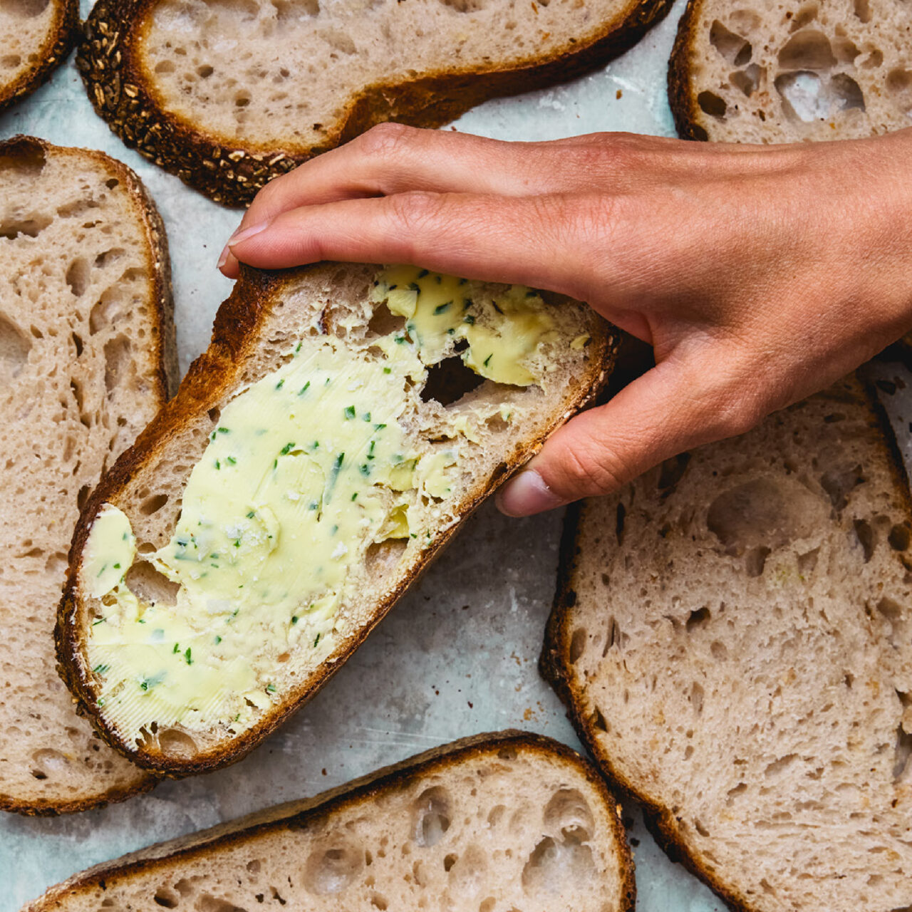 Valokuvassa leipäsiivuja ja käsi tarttumassa voideltuun leipään.